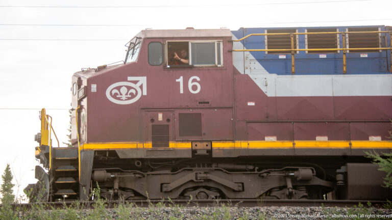 Close side view of maroon-and-gray diesel locomotive number 16 with engineer visible in the cab.