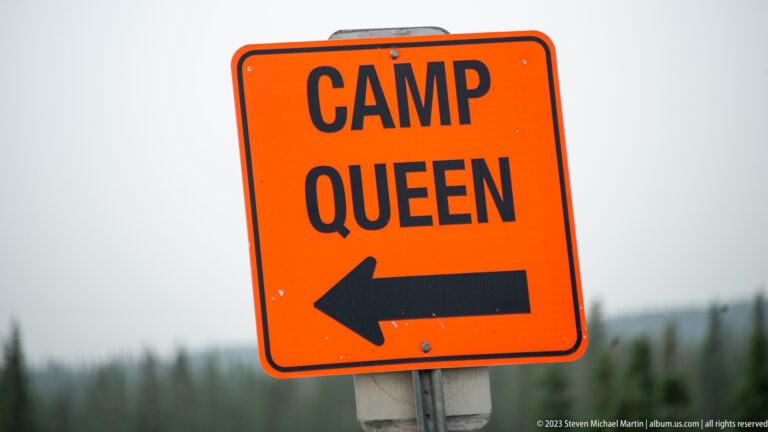 Fluorescent orange sign reading “CAMP QUEEN” with a large black arrow pointing left.