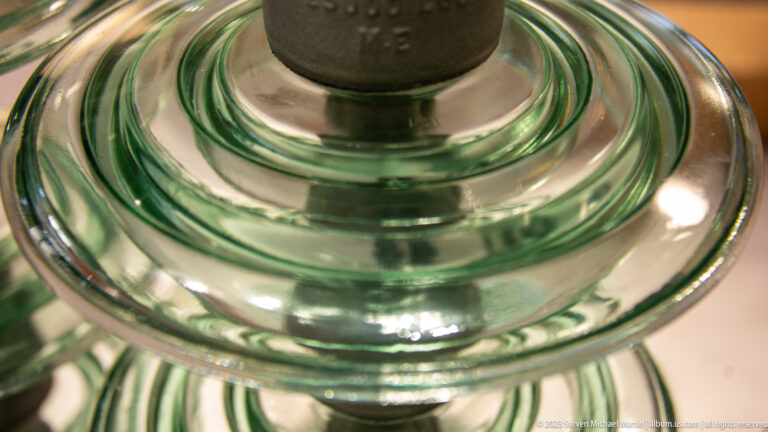 Close view of a green glass electrical insulator with concentric ridges and a dark metal fitting at the top.