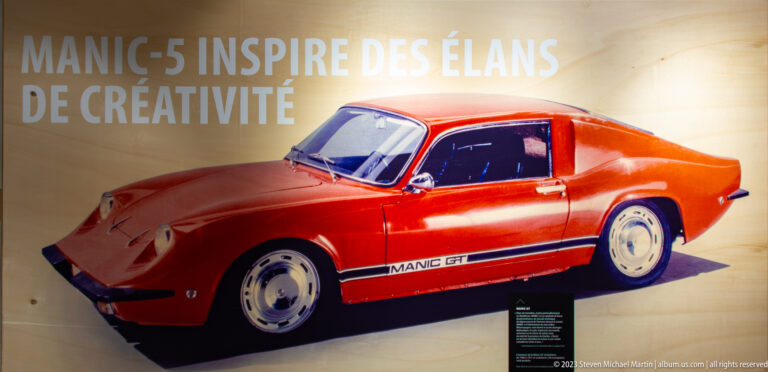 Red Manic GT sports coupe displayed indoors beneath large French text about creativity.