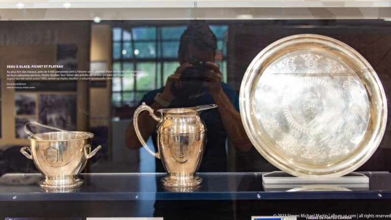 Two polished silver presentation cups and a large round silver tray displayed behind glass.