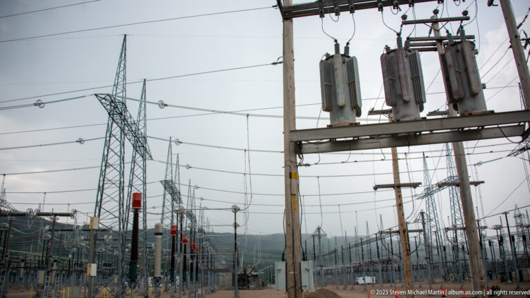 High-voltage electrical switchyard with lattice towers, conductors, insulators, and large suspended equipment at Manic-5.