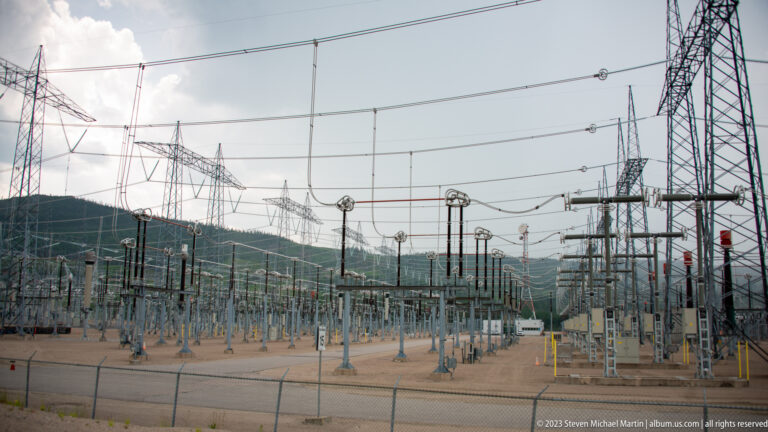 Wide Manic-5 electrical substation with rows of equipment, overhead conductors, and tall transmission towers.