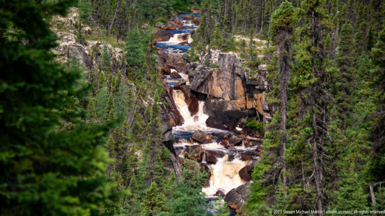 Narrow whitewater cascade descending through fractured bedrock in a densely forested gorge.