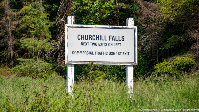 White roadside sign reading “CHURCHILL FALLS,” with exit directions for regular and commercial traffic.