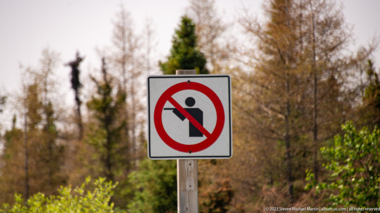 White roadside sign with a black pictogram crossed by a red prohibition circle and diagonal slash.