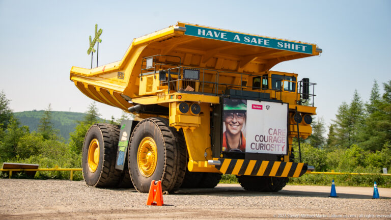 Massive yellow mining haul truck on display with oversized tires and the words “HAVE A SAFE SHIFT” above the cab.