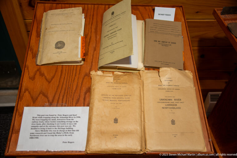 Historic books and mining reports, including worn paper volumes, displayed beneath glass on a wooden surface.