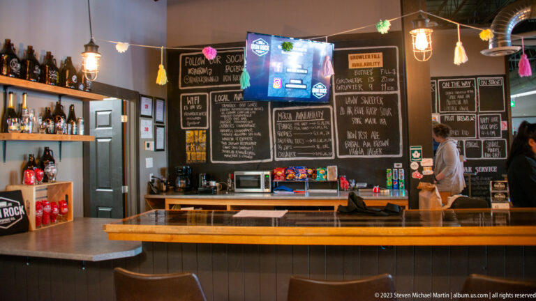 Brewery counter beneath several handwritten chalkboard menus listing beers and prices.