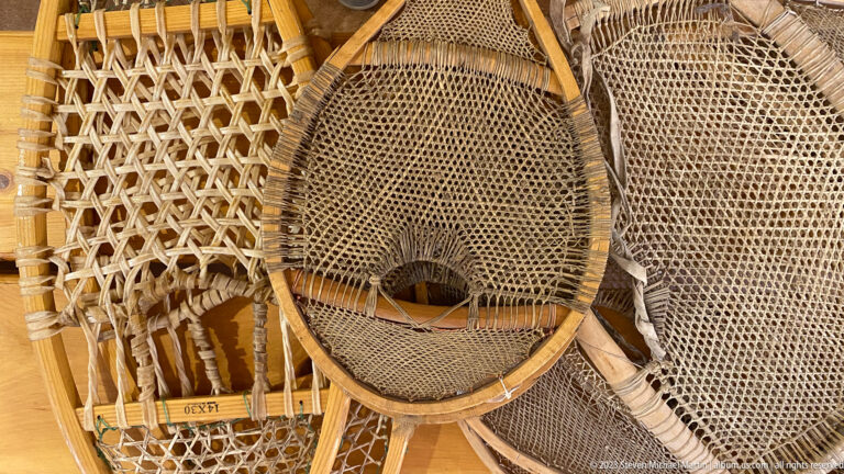 Cluster of traditional wooden snowshoes with woven webbing and varied frame shapes.