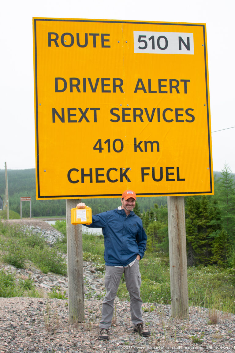 Traveler standing beneath a yellow Route 510 North sign warning that the next services are 410 kilometers away.