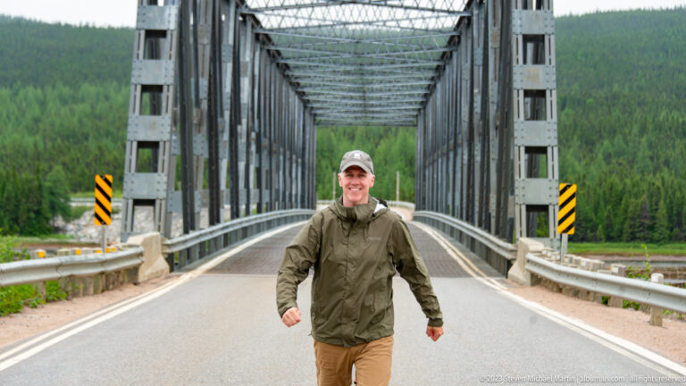 Traveler walking toward the camera on the centerline of a steel through-truss bridge.
