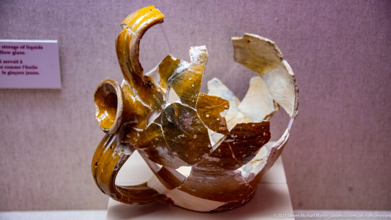 Reconstructed brown-glazed ceramic jug made from surviving sherds around a clear support, with large missing areas.