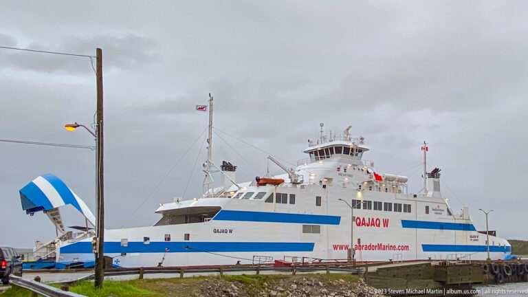 White and blue Qajaq W roll-on/roll-off ferry moored at a Labrador port under gray skies.