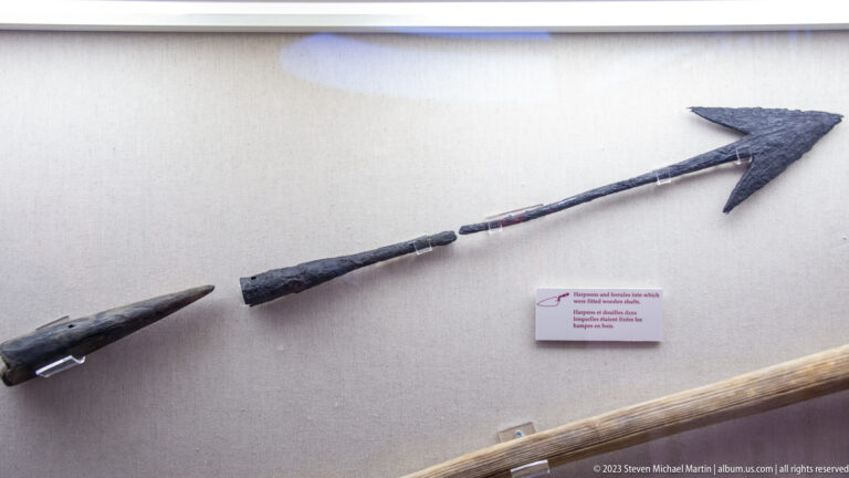 Long wooden-shafted whaling harpoon and lance components with dark iron points mounted on a museum wall.