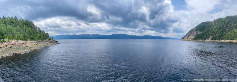 Wide Saguenay Fjord between steep forested rocky headlands under dramatic clouds.