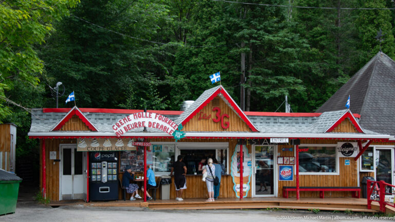 Colorful red-trimmed roadside shop with ice-cream signs, service window, and several visitors.