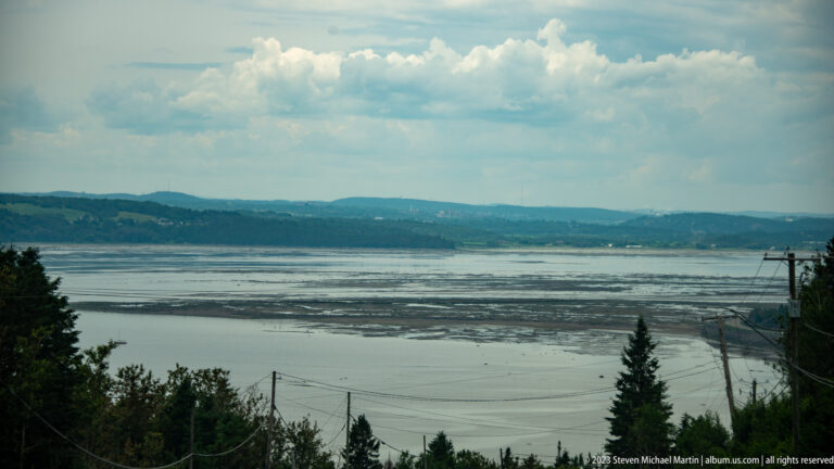 Wide shallow river basin with tidal flats, distant wooded hills, and utility lines in the foreground.