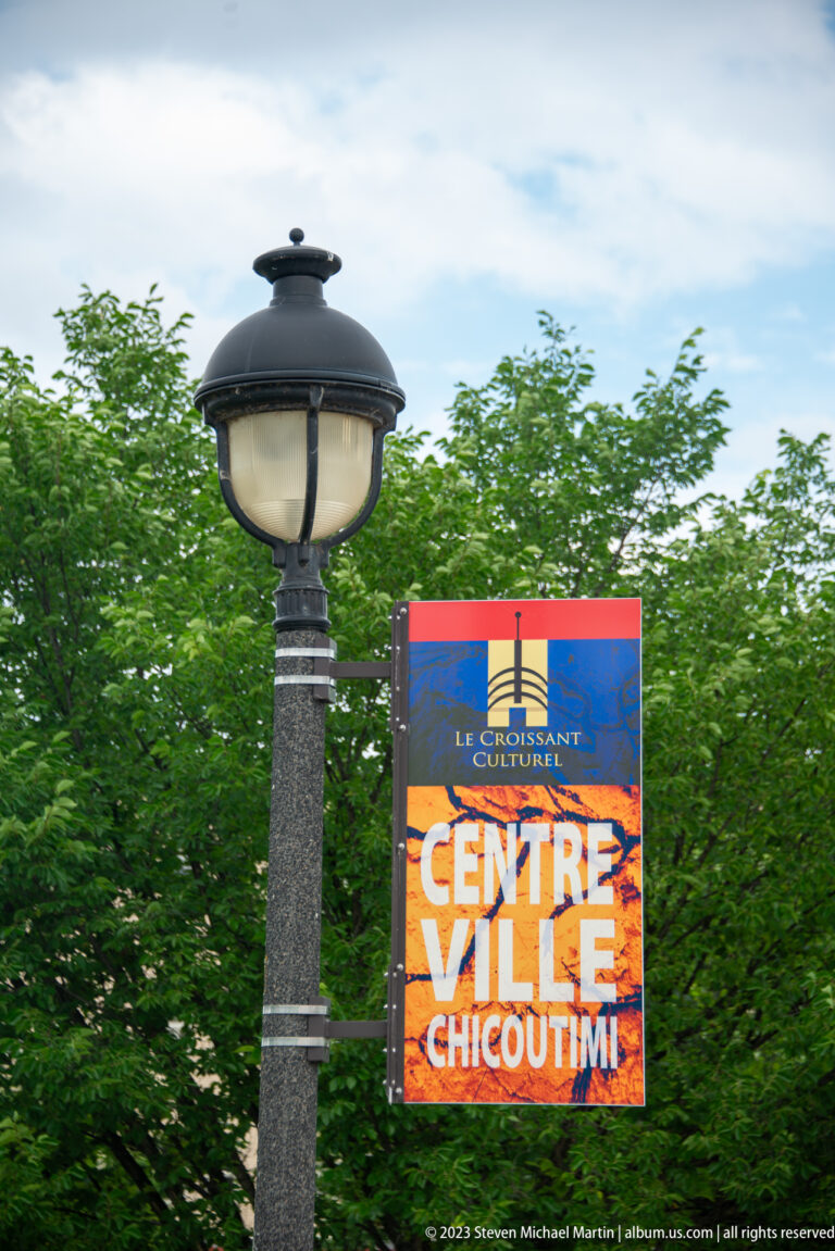 Decorative lamp post carrying a colorful banner reading “Centre Ville Chicoutimi.”