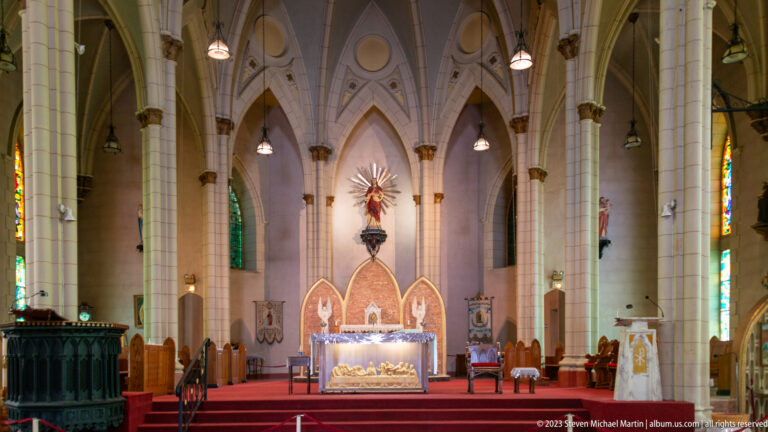 Neo-Gothic church nave with pointed arches, clustered columns, red carpet, altar, and stained-glass windows.