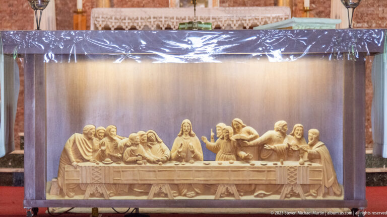 Pale carved Last Supper relief showing Christ and the apostles seated around a long table under protective covering.