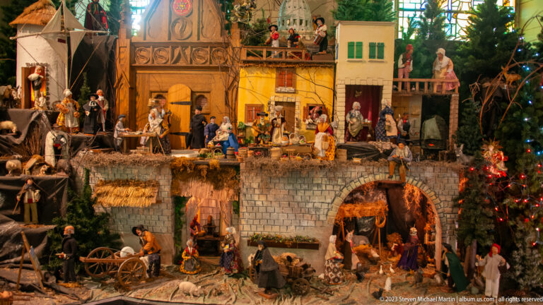 Large multi-level Nativity display with many figures, village buildings, manger scene, and decorated Christmas tree.