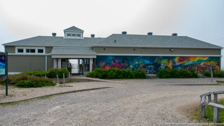 Low gray visitor-centre building with a covered entrance and a long colorful marine mural across the façade.