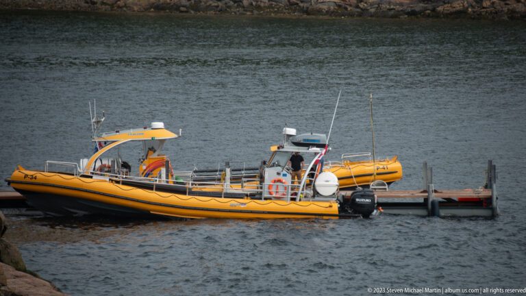 Yellow rigid inflatable boat with twin outboards and open deck moored beside a floating dock.