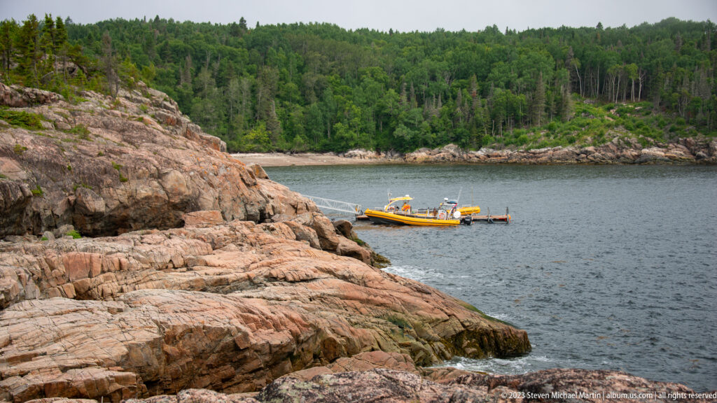 Yellow boat moored in a small cove surrounded by broad rocky ledges and dense forest.