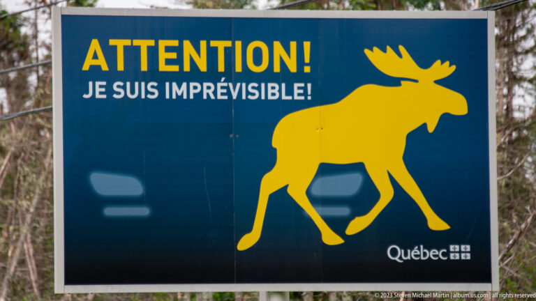 Blue Québec sign with a yellow moose and the French warning “ATTENTION! JE SUIS IMPRÉVISIBLE!”