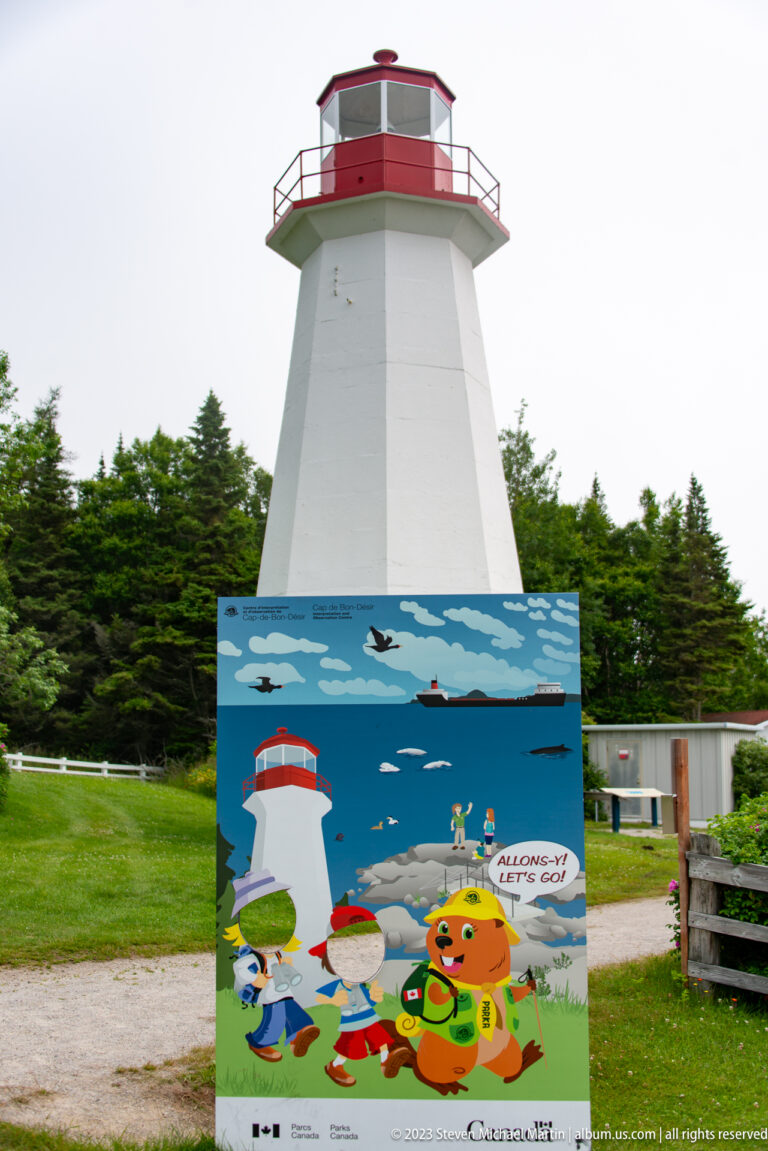 Red-and-white lighthouse behind a colorful illustrated panel with cartoon visitors and marine animals.