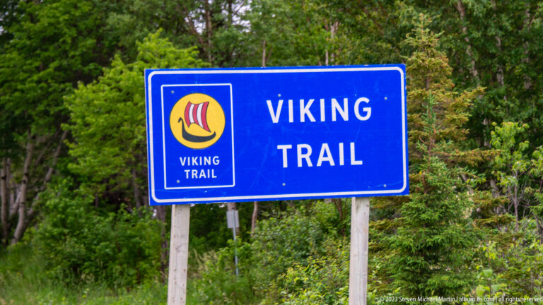 Blue ‘Viking Trail’ roadside sign with Viking-ship emblem in front of leafy forest.