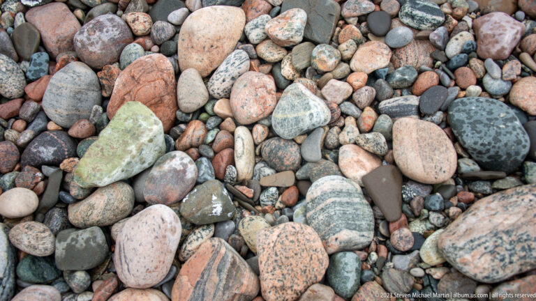 Close view of rounded beach cobbles in pink, green, gray, black, and cream with varied veins and banding.