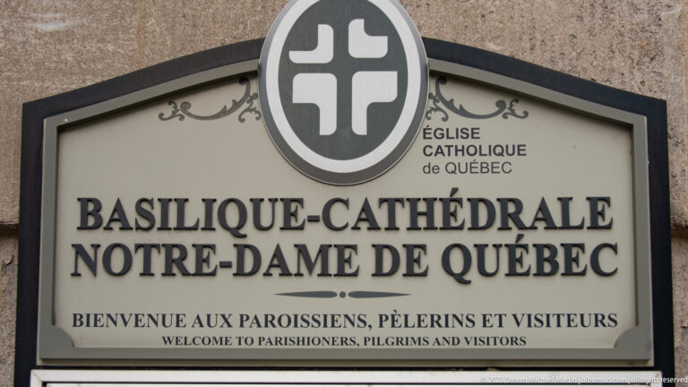 Bilingual sign reading Basilique-Cathédrale Notre-Dame de Québec beneath a circular Catholic Church of Québec emblem.