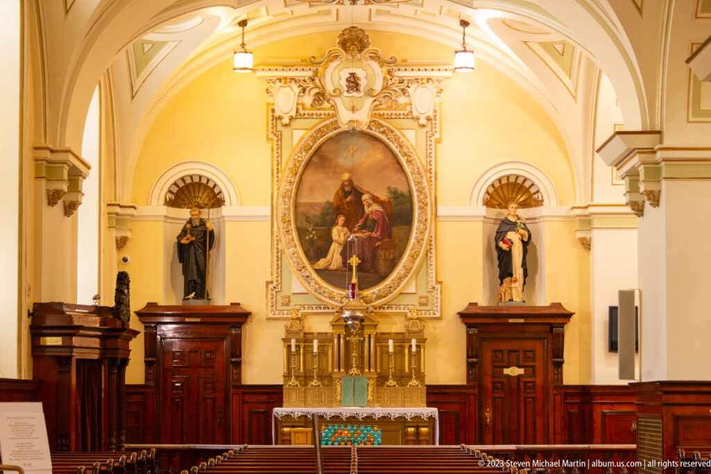 Side altar with an oval religious painting, gilded altar furnishings, and dark-robed saint statues standing in niches on both sides.