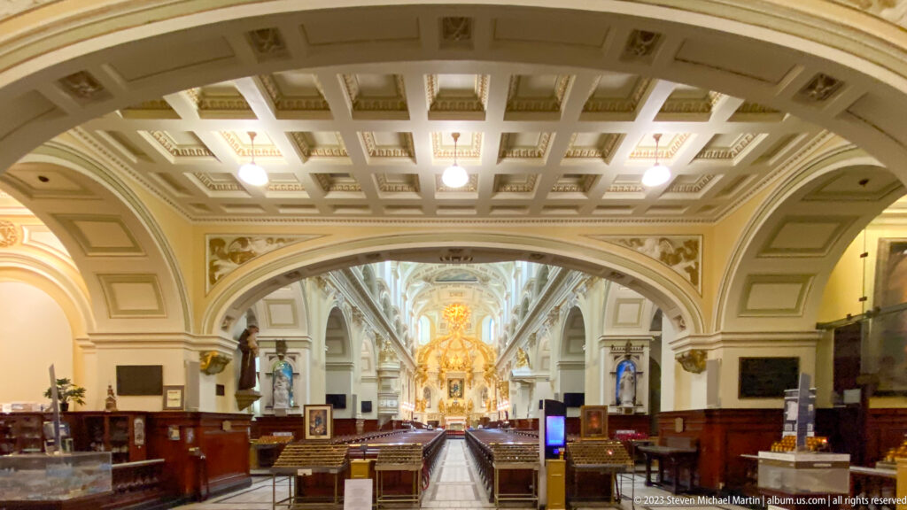 Nave of Notre-Dame de Québec framed by a large coffered arch, with central aisle, side furnishings, and gilded sanctuary beyond.