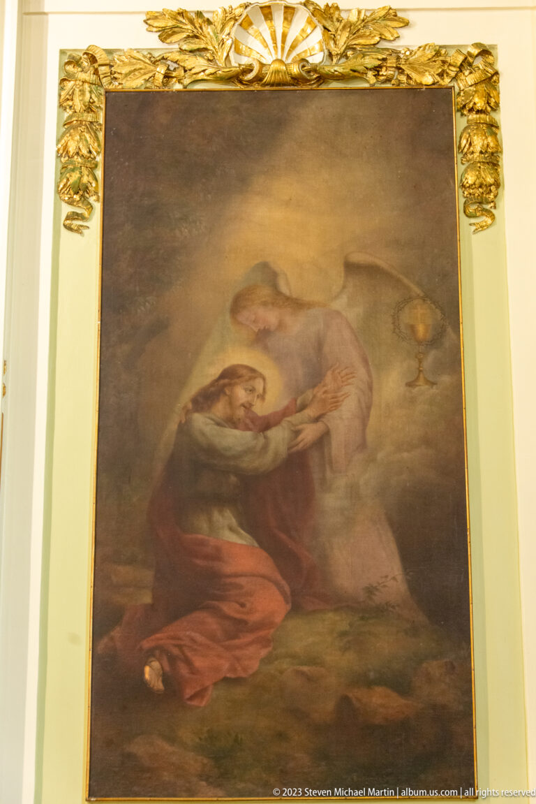 Large religious painting of a kneeling woman in red before a pale-robed sacred figure, set within gilded architectural trim.