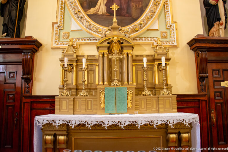 Close side altar with gilded tabernacle, paired candlesticks, lace altar cloth, turquoise frontal detail, and dark wood surround.