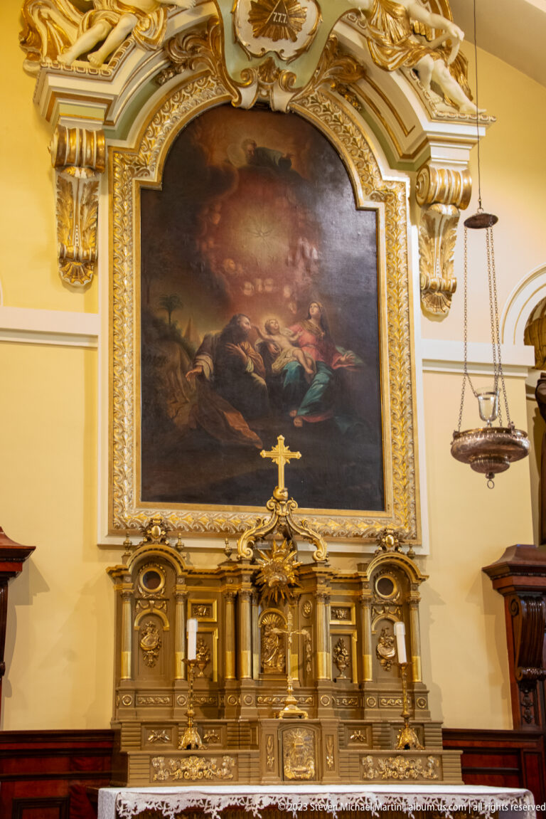 Large religious painting above an ornate gilded side altar with tabernacle and hanging sanctuary lamps.