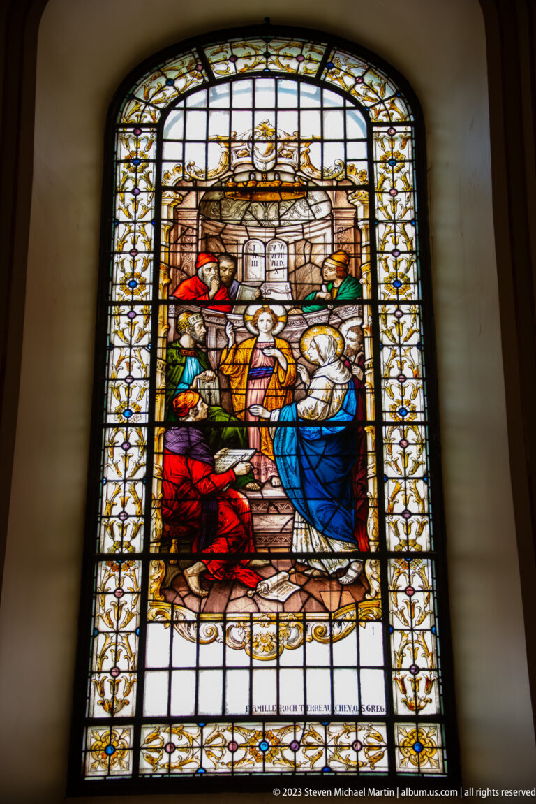 Stained-glass window with clerical and lay figures surrounding a central blue-and-white-robed woman.