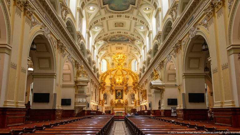 Symmetrical view down the nave of Notre-Dame de Québec toward a gilded sanctuary, with wooden pews, arcades, and decorated ceiling.