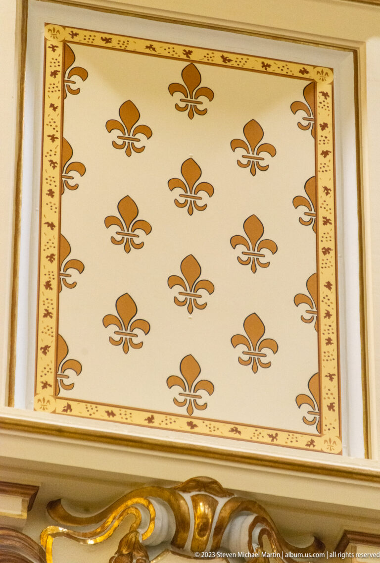Cream rectangular panel patterned with repeated gold fleur-de-lis motifs and a narrow decorative border.