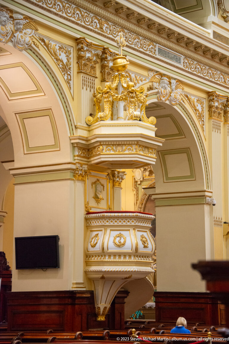 Ornate cream-and-gold elevated pulpit with curved box and sculpted canopy attached to a church pier.