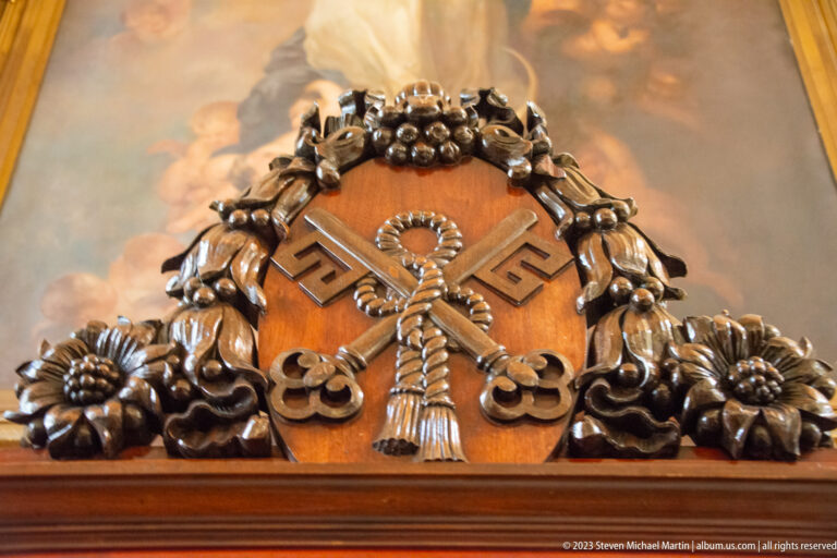 Carved wooden panel with crossed keys, looped cord motif, flowers, leaves, and clustered fruit.