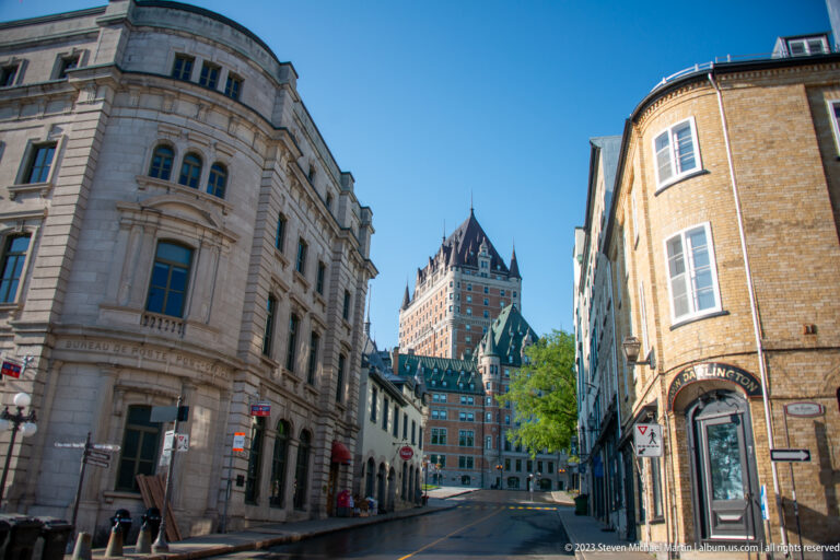 Old Québec street between historic commercial buildings leading toward the Château Frontenac under a clear blue sky.