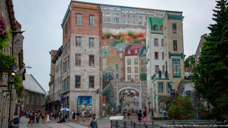 Fresque des Québécois covers a tall building wall with painted architecture and figures as visitors gather below.