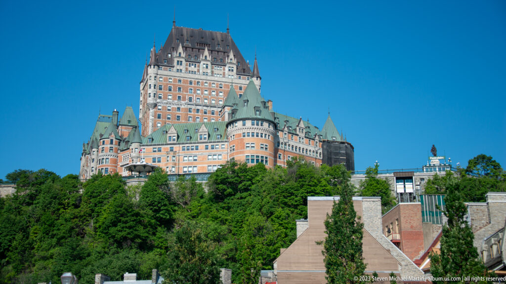 Château Frontenac rising above dense green trees and smaller rooftops, with tall central tower and clustered copper-roofed turrets.