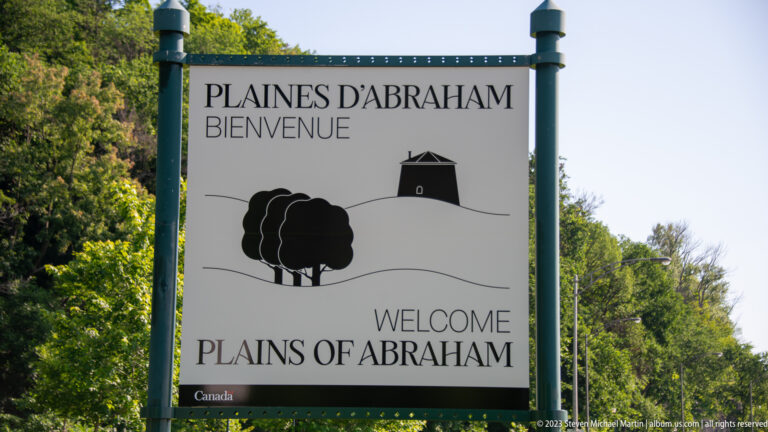 Bilingual Plaines d’Abraham and Plains of Abraham welcome sign with stylized trees and a small historic structure.