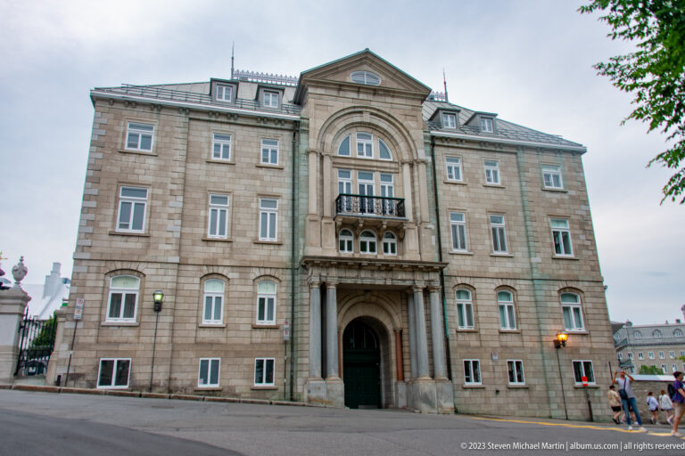 Symmetrical stone institutional building with a deep arched doorway, tall central window bay, classical detailing, and rows of sash windows.