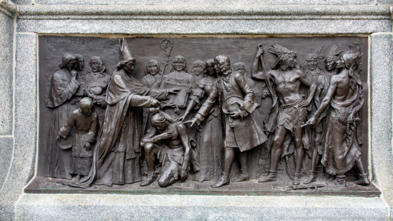 Rectangular bronze bas-relief with many historical figures, gestures, and flags set into a pale stone surround.